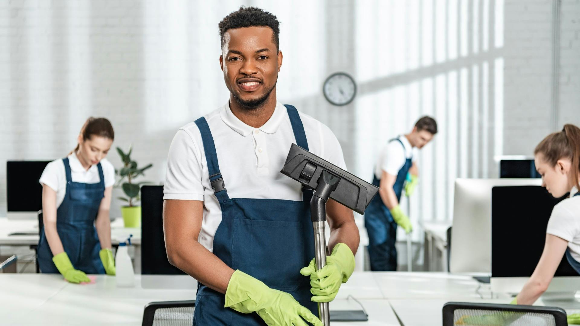 Man holding a vacuum smiling while his crew members clean behind him
