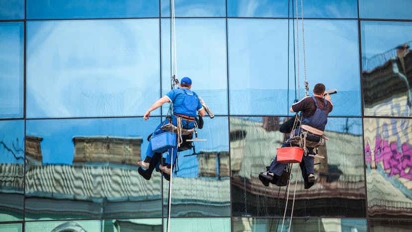 Two commercial window cleaners hanging from a harness to clean a high rise building