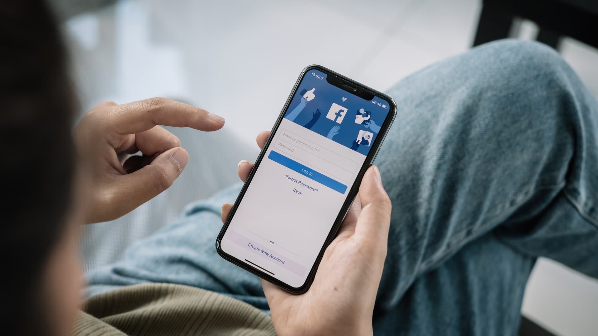 Man sitting down while holding a phone with Facebook login page on phone screen