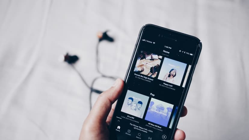 Hand holding phone while displaying album covers with wire headphones in the background