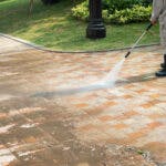man using a pressure washer on driveway of home