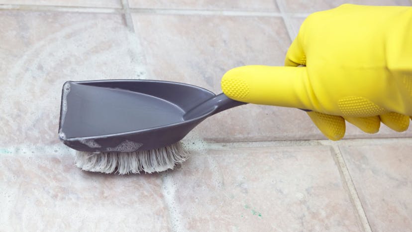 Gloved hand cleaning tile with a brush
