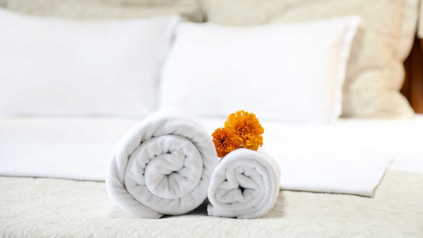 Rolled towels sitting on a bed with a flower placed on top of them