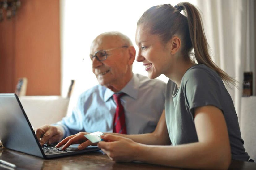 Woman sitting in front of a laptop with her grandfather to her right 