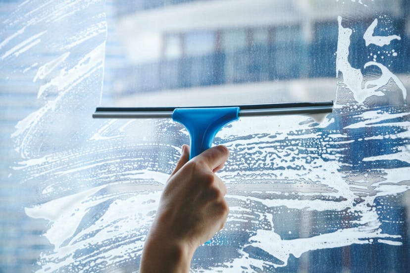 Squeegee wiping away soapy solution from window surface 